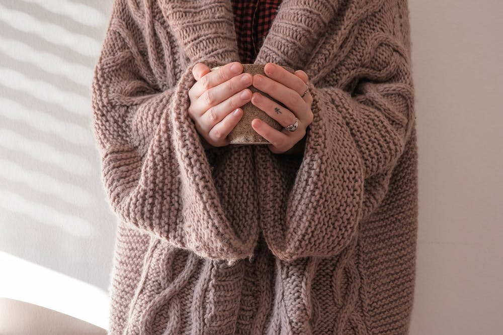 A person wearing a woolly coat holds a cup of tea.
